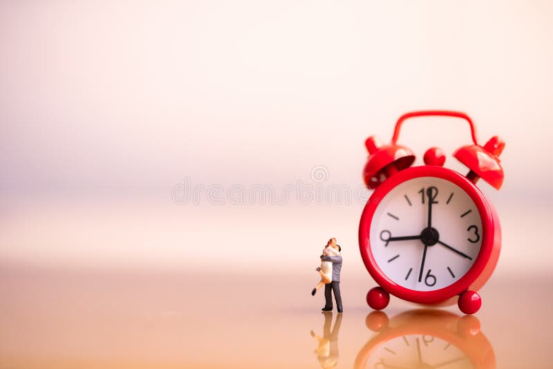 Figuras pequenas dos pares no amor e no despertador vermelho imagem de stock Figuras pequenas dos pares no amor e no despertador vermelho imagem de stock