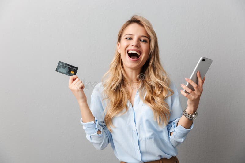 Fijne jonge blonde zakenvrouw met een geïsoleerde grijze achtergrond met een creditcard met mobiele telefoon