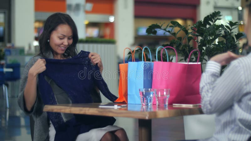 Fijne jonge vrouw met boodschappentassen die nieuwe kleren aan haar vriend tonen