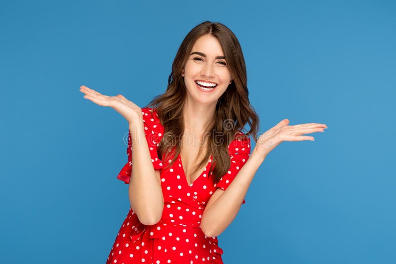 Fijne jonge vrouw met een felle glimlach op een rode jurk die opkijkt tegen een opgewonden gezicht met handen boven de blauwe ach