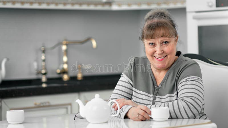 Fijne, plezierige vrouw van middelbare leeftijd die graag thee glimlacht als ze naar camera kijkt