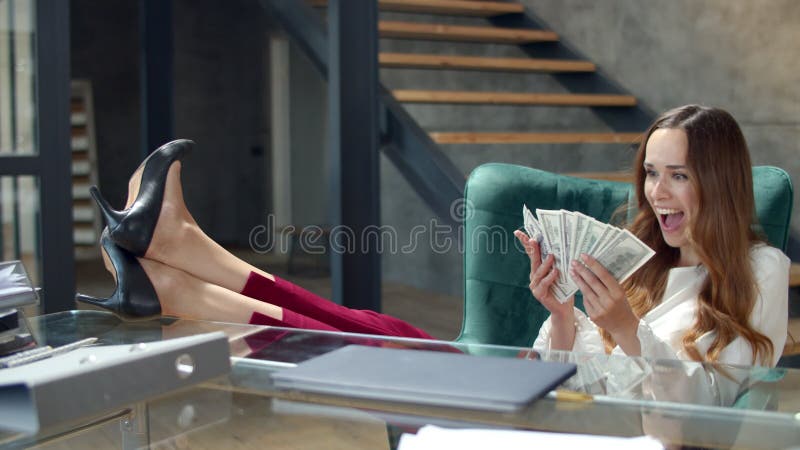 Fijne zakenvrouw die geld houdt met benen op tafel Meisje maakt geld regen