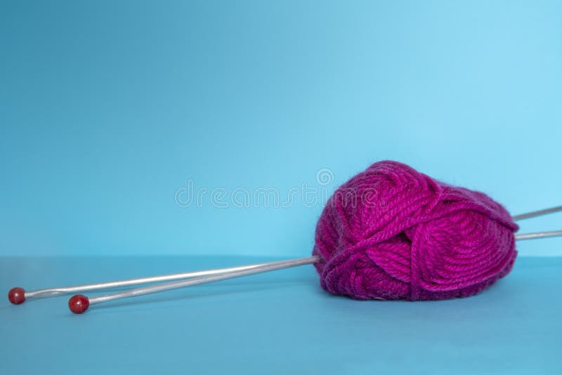 Woolen yarn pink for knitting and 2 needles on blue surface. Selective focus. Copy space for text. Woolen yarn pink for knitting and 2 needles on blue surface. Selective focus. Copy space for text.