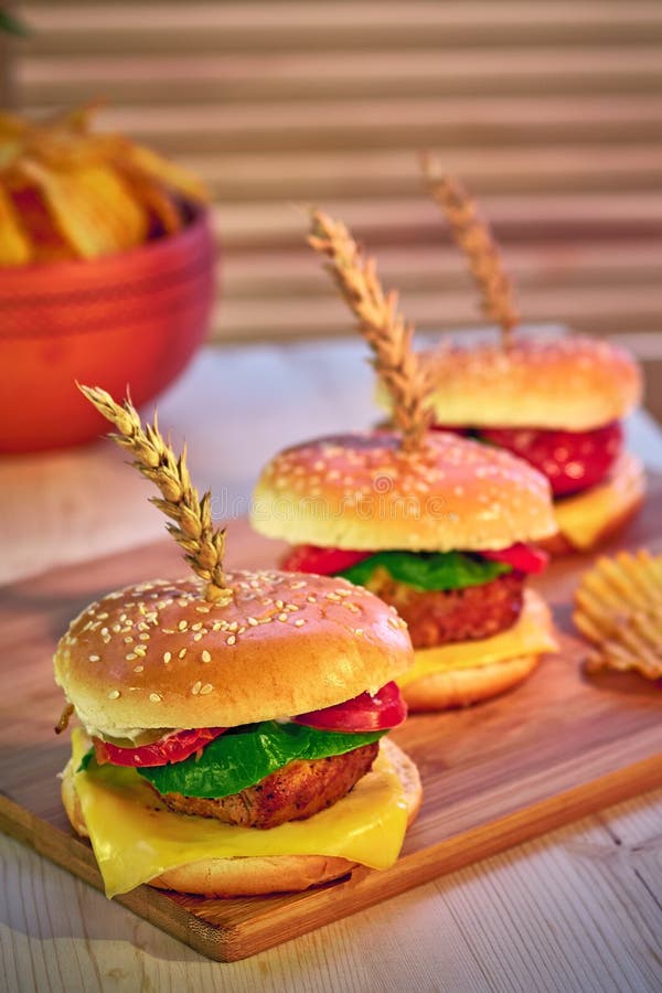 Fila de tres hamburguesas apetitosas de moda en el tablero de madera en restaurante Foco selectivo, perspectiva Alimentos de prep foto de archivo Fila de tres hamburguesas apetitosas de moda en el tablero de madera en restaurante Foco selectivo, perspectiva Alimentos de prep foto de archivo