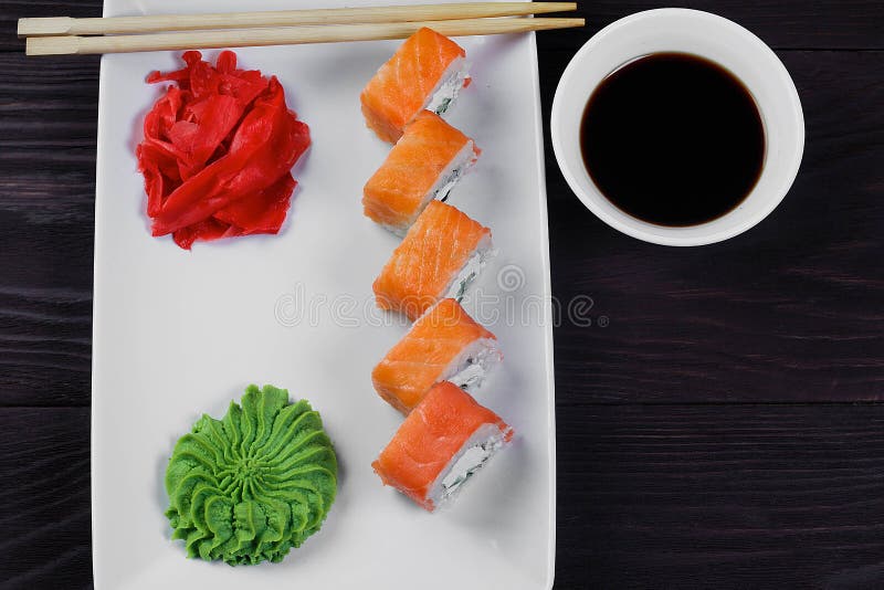 Filadelfia suszi rolki na białego kwadrata talerzu z wasabi, soja kumberlandem i imbirem, drewniany tło zmrok fotografia stock Filadelfia suszi rolki na białego kwadrata talerzu z wasabi, soja kumberlandem i imbirem, drewniany tło zmrok fotografia stock