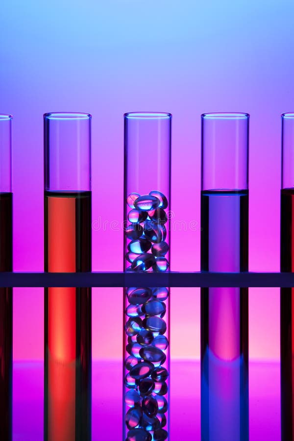 Row of test tubes filled with colored fluid, one filled with gel cap vitamins. Row of test tubes filled with colored fluid, one filled with gel cap vitamins.