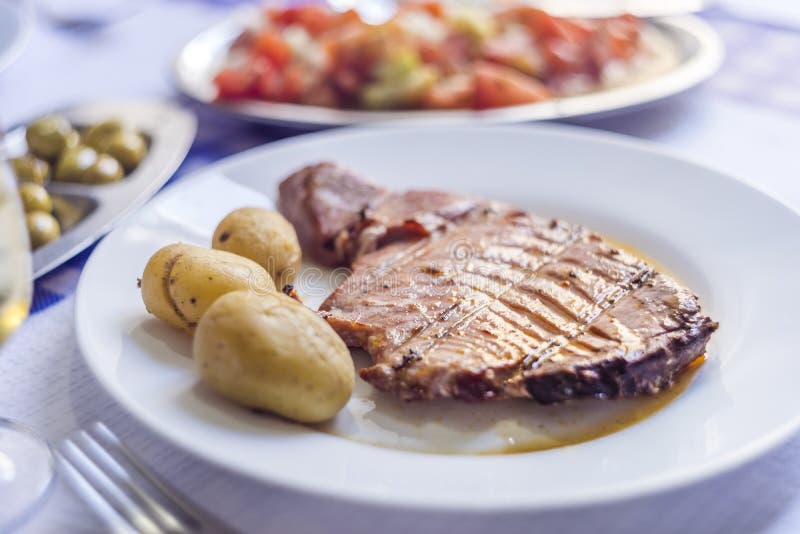 Filete de atún acompañado con las patatas, las aceitunas, la ensalada del tomate y w imagen de archivo libre de regalías Filete de atún acompañado con las patatas, las aceitunas, la ensalada del tomate y w imagen de archivo libre de regalías