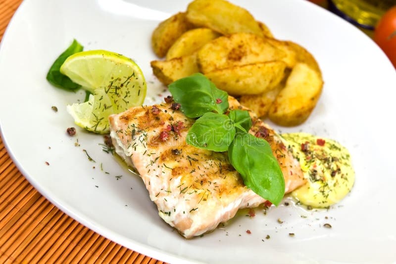 Filete de color salmón asado a la parilla con las cuñas de la patata imagen de archivo Filete de color salmón asado a la parilla con las cuñas de la patata imagen de archivo