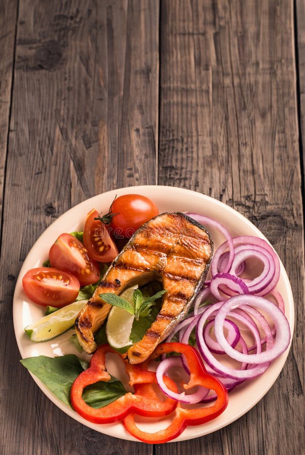 Filete de color salmón asado a la parrilla con la cebolla cortada y los tomates verticales foto de archivo libre de regalías Filete de color salmón asado a la parrilla con la cebolla cortada y los tomates verticales foto de archivo libre de regalías