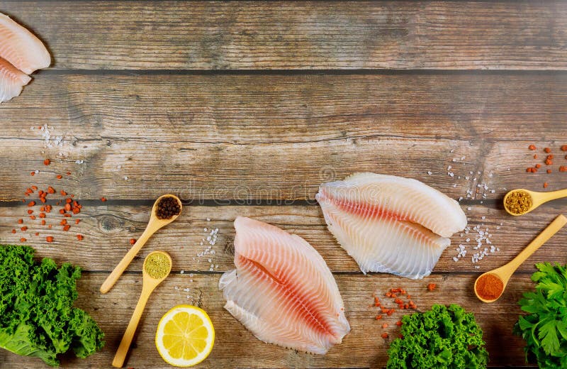 Filete de tilapia de pescado sin cocer sobre la mesa con limón y especias imagenes de archivo