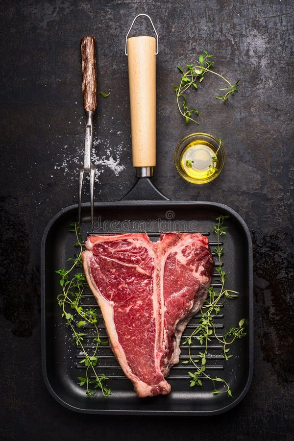 filete del T-hueso en freír la cacerola de la parrilla con la bifurcación, el aceite y el aderezo de la carne en fondo rústico os imagen de archivo libre de regalías filete del T-hueso en freír la cacerola de la parrilla con la bifurcación, el aceite y el aderezo de la carne en fondo rústico os imagen de archivo libre de regalías
