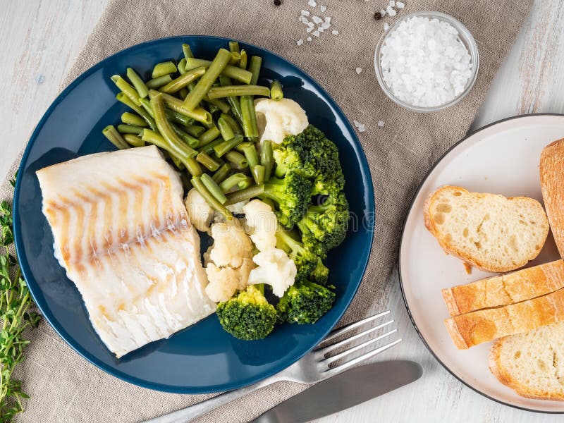 Filetto di merluzzo al forno del pesce di mare con le verdure sul piatto blu, pane, fotografie stock Filetto di merluzzo al forno del pesce di mare con le verdure sul piatto blu, pane, fotografie stock