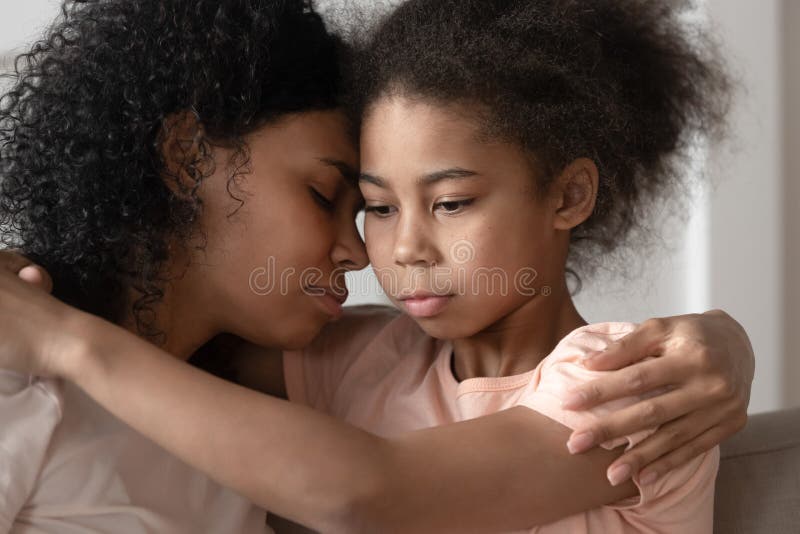 Filha afro-americano pensativa da criança que abraça a ligação da mamã que afaga