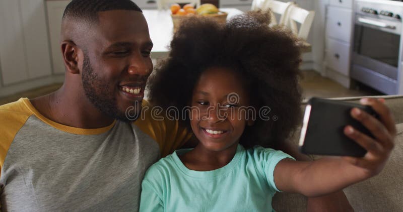 A filha americana africana e seu pai juntos sentando no sofá sorrindo