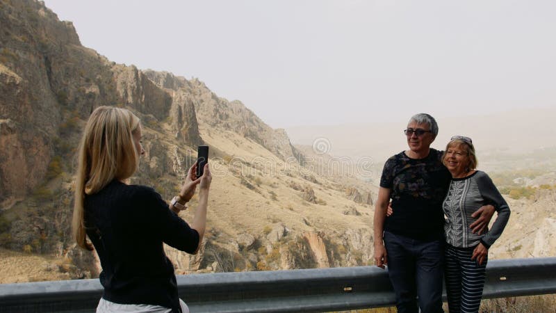 Filha que toma a foto pelo telefone celular de seus pais superiores na viagem das férias nas montanhas na parada da estrada Famíl