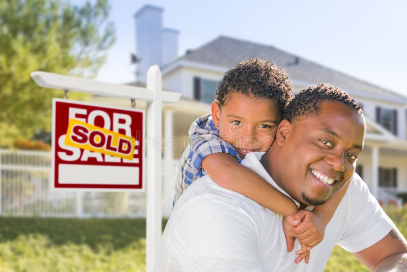 African American Father and Mixed Race Son In Front of Sold Home For Sale Real Estate Sign and New House. African American Father and Mixed Race Son In Front of Sold Home For Sale Real Estate Sign and New House.