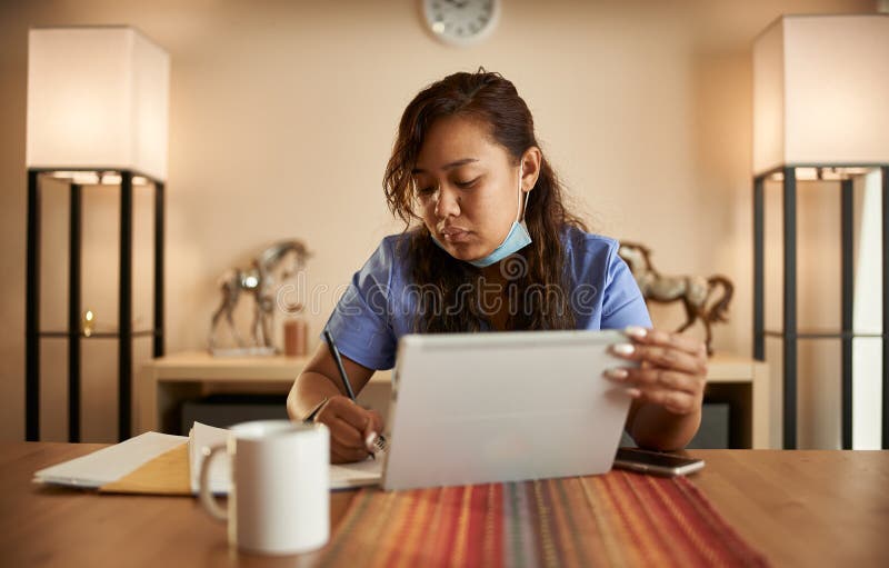 Filipina Nurse Working from Home Doing Paperwork and Using Tablet Stock