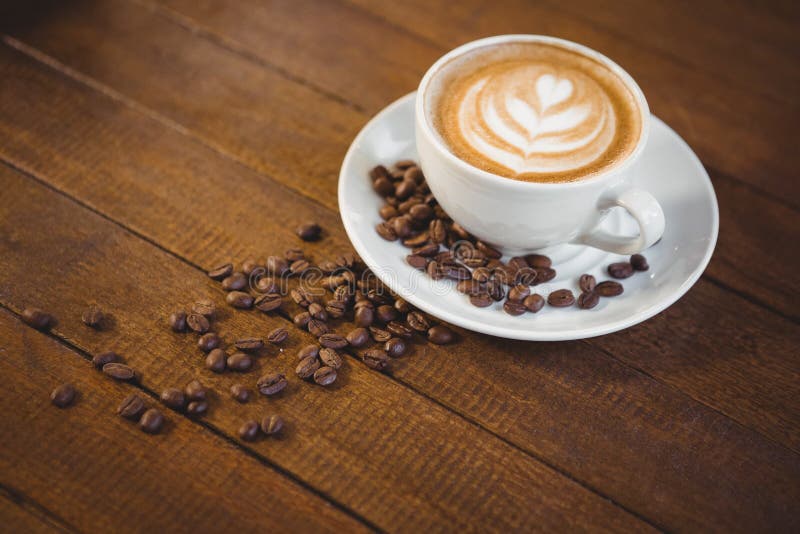 Filiżanka cappuccino z kawową sztuką i kawowymi fasolami