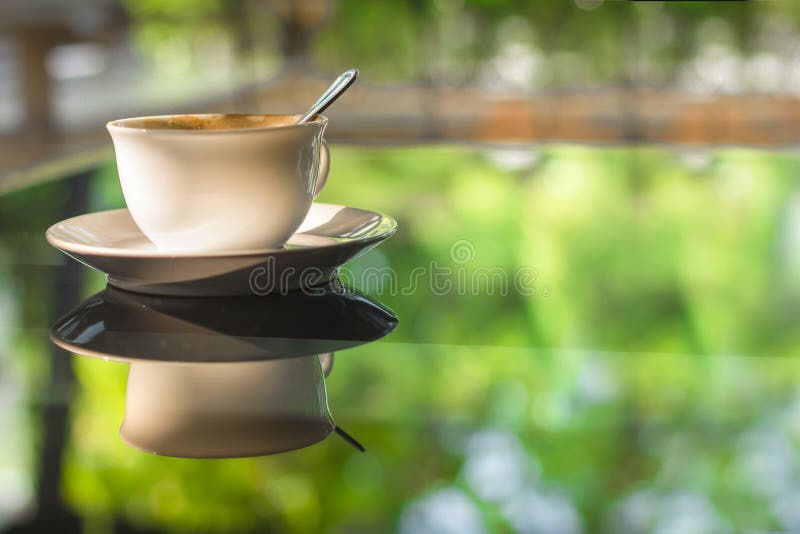 Filiżanka kawy na lustrzanym szkło stole odbija zielonego lato ogród