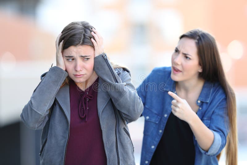 Angry girl accusing her sad friend who is covering ears walking in the street. Angry girl accusing her sad friend who is covering ears walking in the street