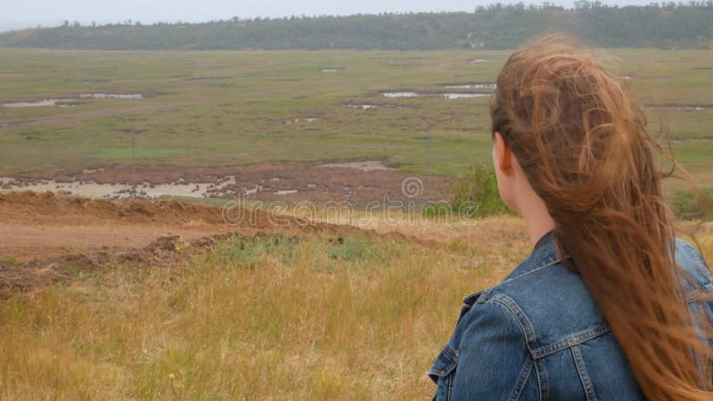 Fille adorable dans la vue arrière de chemise de denim sur une colline avec l'herbe jaune. Femme élégante avec de longs cheveux bl clips vidéos