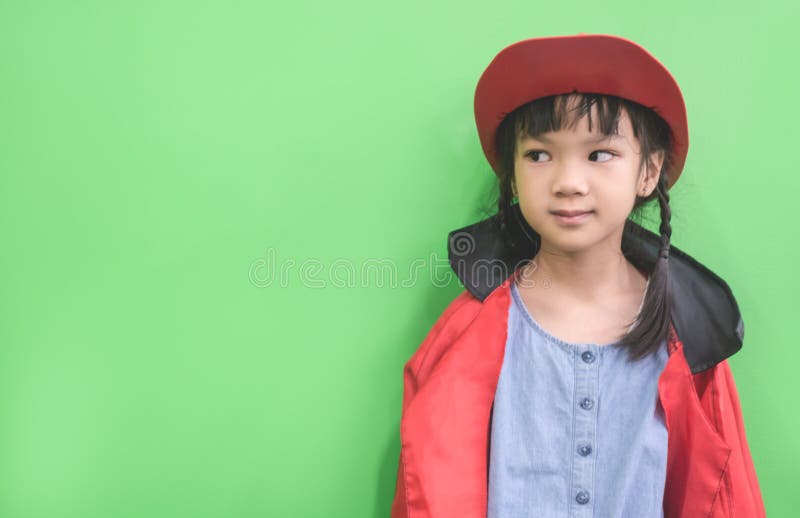 Fille asiatique mignonne dans la veste de pluie regardant vers la gauche sur le vert image stock Fille asiatique mignonne dans la veste de pluie regardant vers la gauche sur le vert image stock