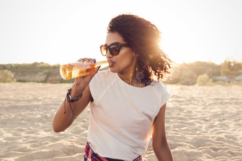 Fille assez africaine de jeunes dans des lunettes de soleil buvant de la bière photos libres de droits Fille assez africaine de jeunes dans des lunettes de soleil buvant de la bière photos libres de droits