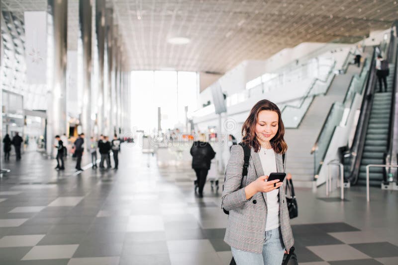 Fille aux promenades d'aéroport regardant son smartphone image libre de droits Fille aux promenades d'aéroport regardant son smartphone image libre de droits