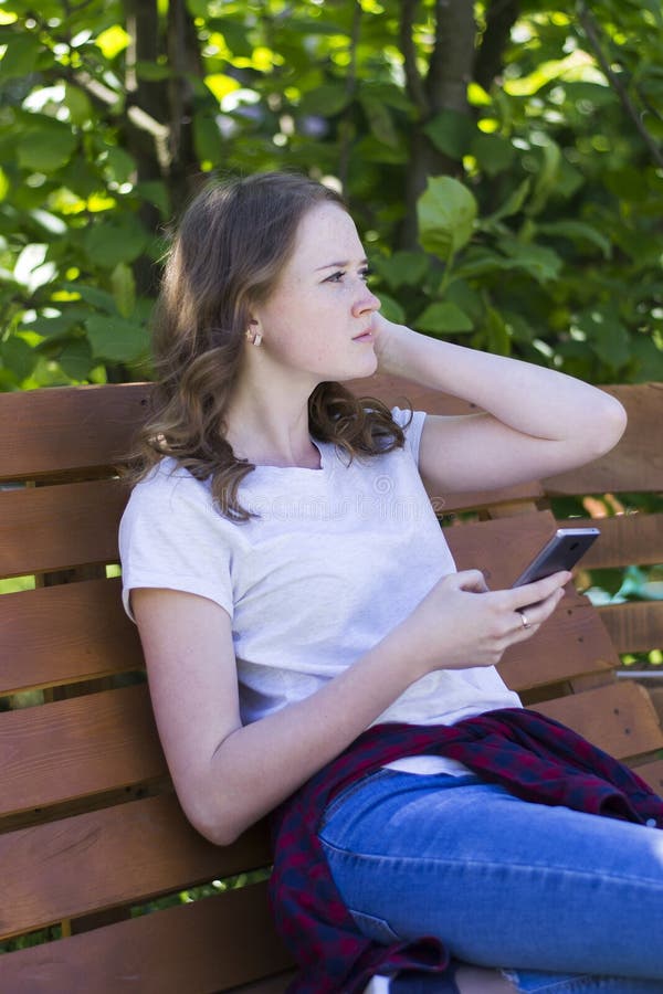 Fille avec un téléphone sur un banc images libres de droits Fille avec un téléphone sur un banc images libres de droits
