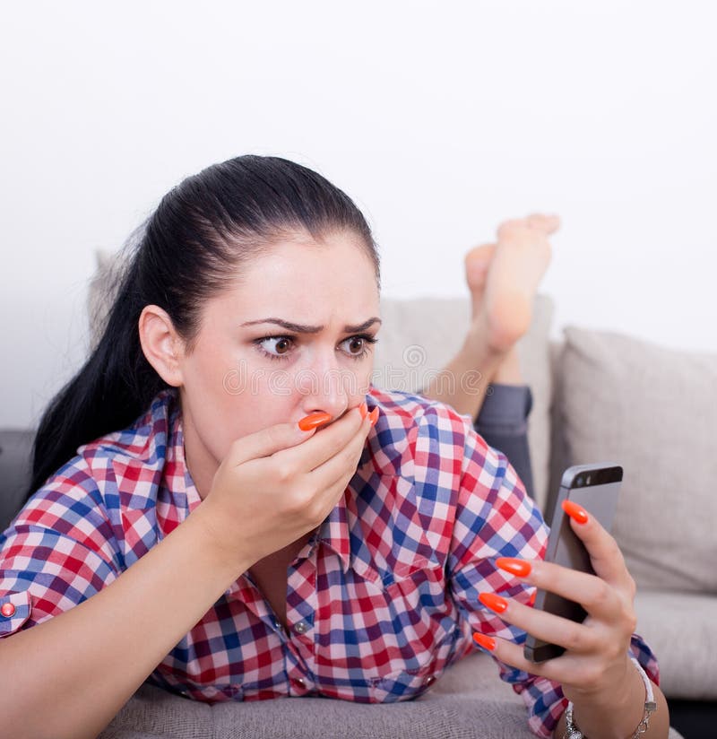 Fille choquée avec le téléphone portable sur le sofa image stock Fille choquée avec le téléphone portable sur le sofa image stock