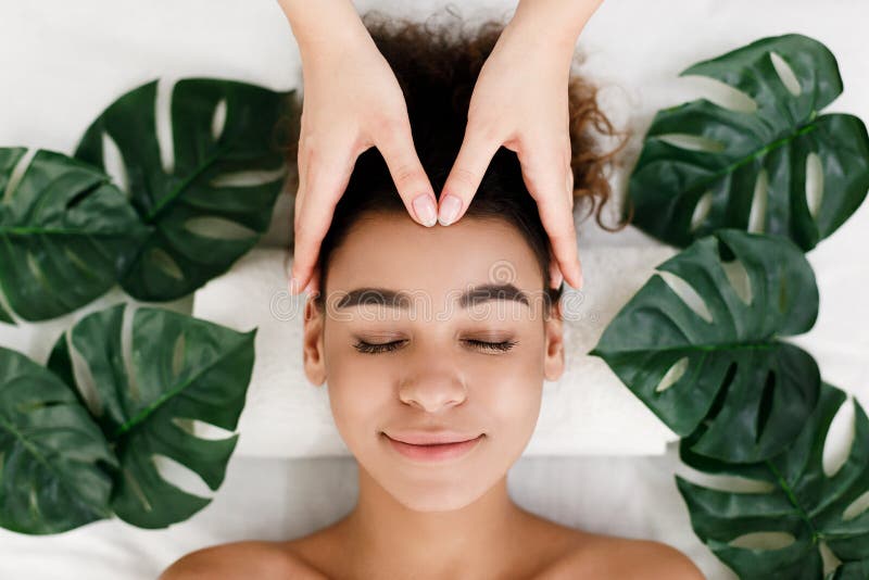 Fille d'afro-américain obtenant le massage facial avec les feuilles tropicales autour images stock Fille d'afro-américain obtenant le massage facial avec les feuilles tropicales autour images stock