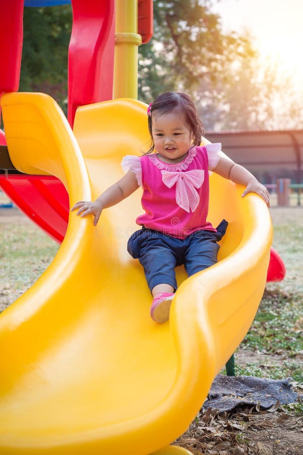 Fille d'enfant en bas âge jouant sur une glissière au terrain de jeu d'enfants photo libre de droits Fille d'enfant en bas âge jouant sur une glissière au terrain de jeu d'enfants photo libre de droits