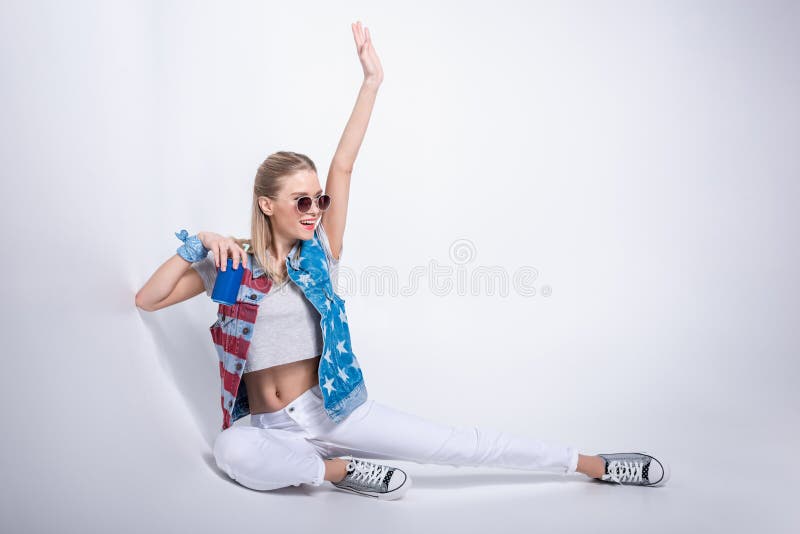 Fille dans des lunettes de soleil portant le gilet de denim avec la bannière étoilée et buvant la soude de la boîte en aluminium photos libres de droits Fille dans des lunettes de soleil portant le gilet de denim avec la bannière étoilée et buvant la soude de la boîte en aluminium photos libres de droits