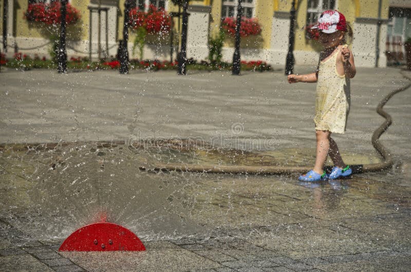 Fille dans la ville chaude d'été avec l'arroseuse de l'eau image libre de droits Fille dans la ville chaude d'été avec l'arroseuse de l'eau image libre de droits