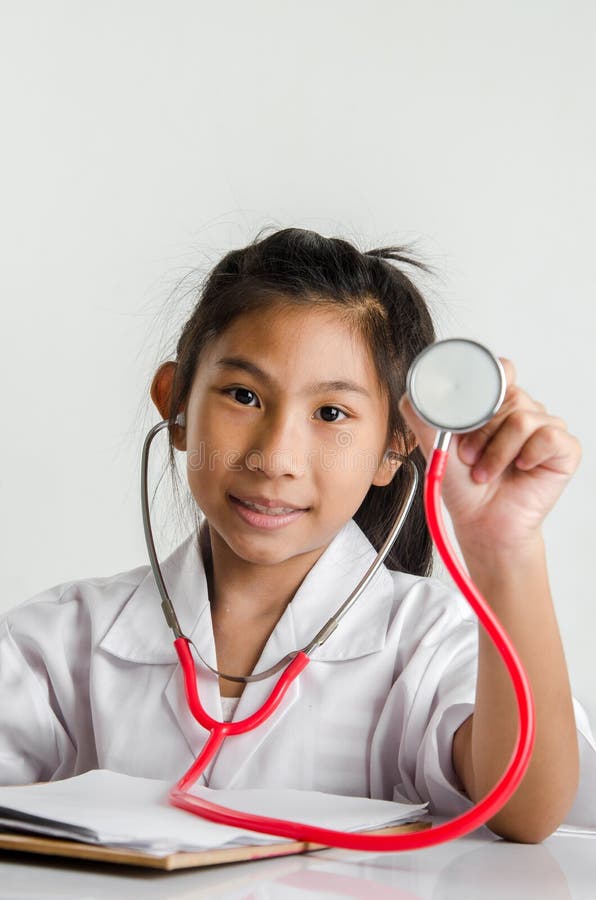 Fille dans le costume de docteur tenant le stéthoscope rouge sur le backgroun gris photo stock Fille dans le costume de docteur tenant le stéthoscope rouge sur le backgroun gris photo stock