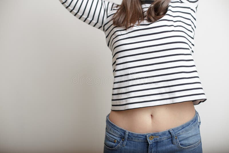 Young girl in blue jeans and a striped sweater and lifted her arms bare belly with a beautiful waist and umbilicus. Young girl in blue jeans and a striped sweater and lifted her arms bare belly with a beautiful waist and umbilicus