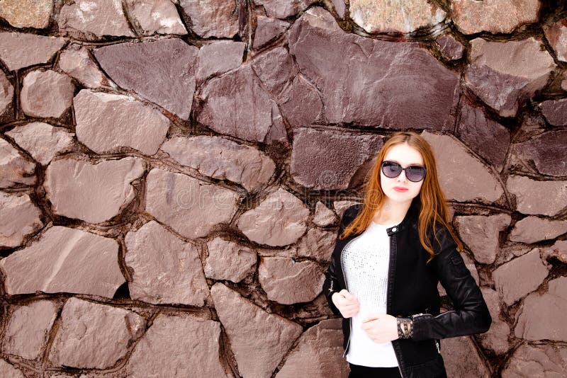 Fille dans les lunettes de soleil et la veste noires au-dessus d'un mur de briques photo stock Fille dans les lunettes de soleil et la veste noires au-dessus d'un mur de briques photo stock