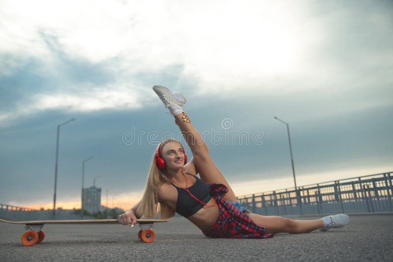 Fille dans une chemise rouge au coucher du soleil avec le patin et les écouteurs photographie stock Fille dans une chemise rouge au coucher du soleil avec le patin et les écouteurs photographie stock
