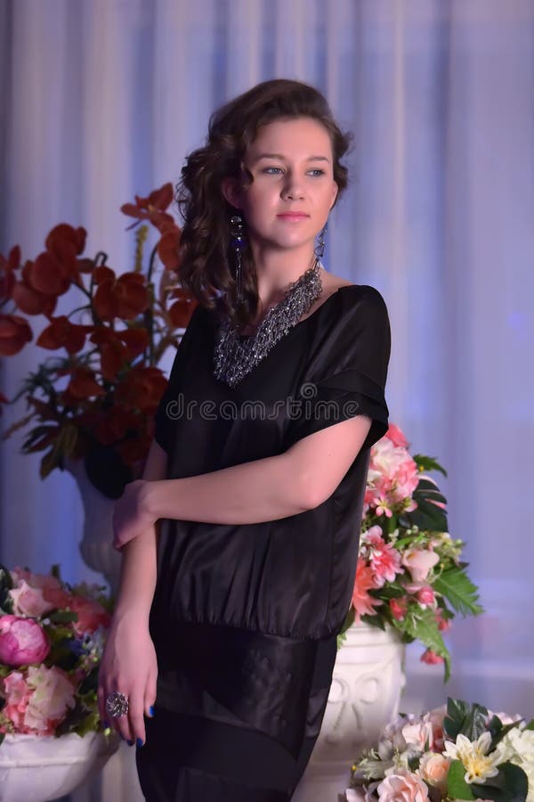Fille dans une robe noire à côté d'un vase avec des fleurs image libre de droits Fille dans une robe noire à côté d'un vase avec des fleurs image libre de droits
