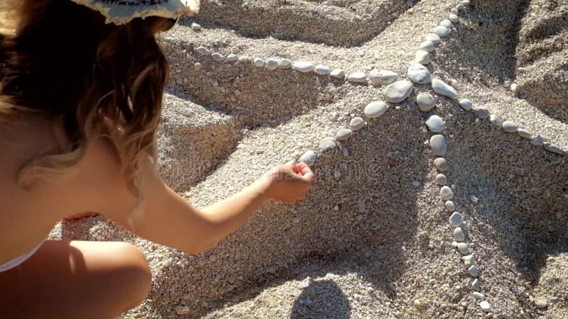 Fille de beauté faisant des étoiles de mer du sable se reposant à la plage