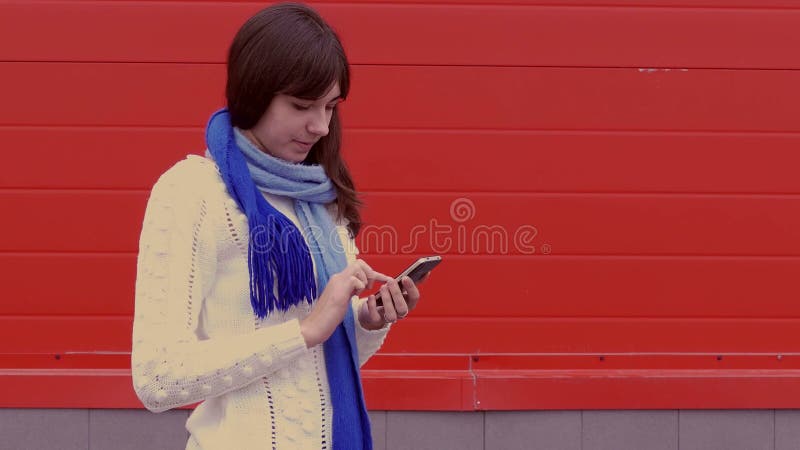 Fille de femme tenant un téléphone de smartphone dans le media social de réseaux d'une veste et d'une écharpe banque de vidéos