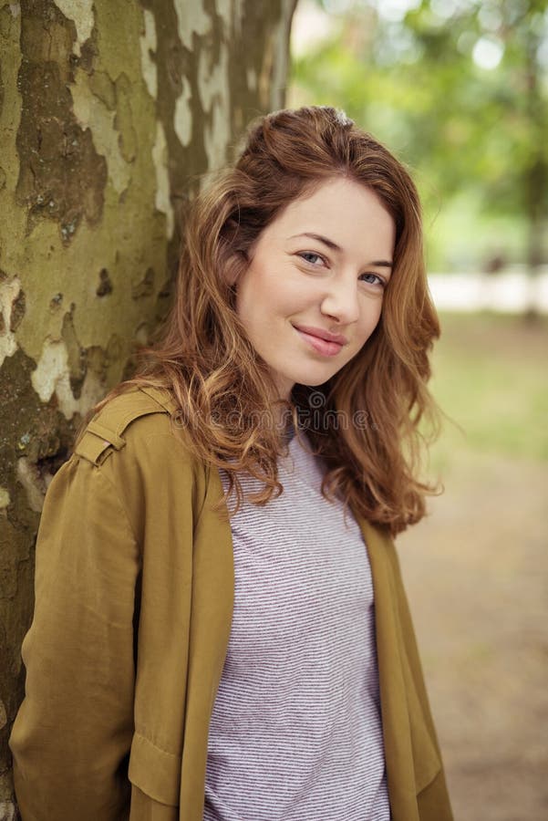 Fille de l'adolescence de sourire se penchant contre le tronc d'arbre photo libre de droits Fille de l'adolescence de sourire se penchant contre le tronc d'arbre photo libre de droits