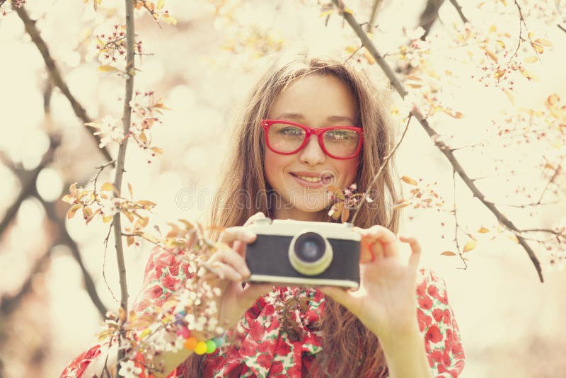 Fille de l'adolescence en verres avec l'appareil-photo de vintage près de l'arbre de fleur image libre de droits Fille de l'adolescence en verres avec l'appareil-photo de vintage près de l'arbre de fleur image libre de droits