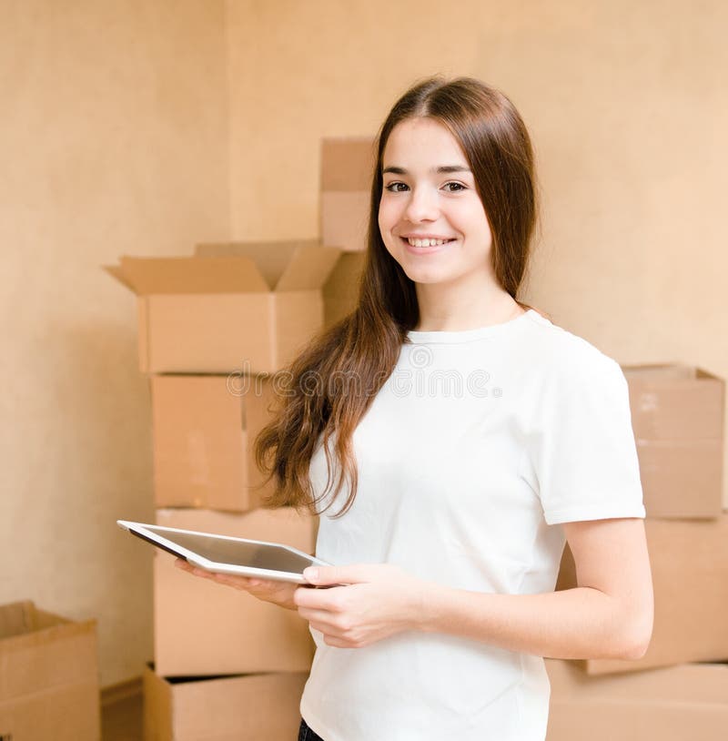 Fille de l'adolescence heureuse avec la tablette se tenant sur un fond des boîtes images stock Fille de l'adolescence heureuse avec la tablette se tenant sur un fond des boîtes images stock