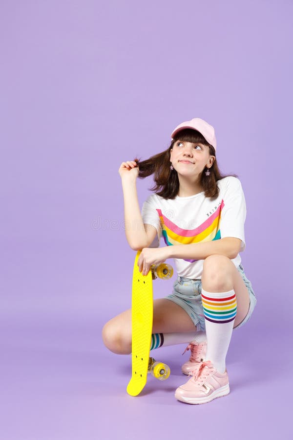 Fille de l'adolescence songeuse dans des v?tements vifs se reposant tenant la planche ? roulettes jaune, recherchant d'isolement image libre de droits Fille de l'adolescence songeuse dans des v?tements vifs se reposant tenant la planche ? roulettes jaune, recherchant d'isolement image libre de droits