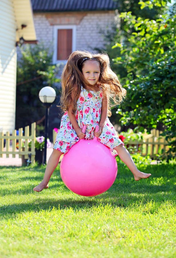 Cute four-year girl bouncing on a big ball in a front yard. Cute four-year girl bouncing on a big ball in a front yard