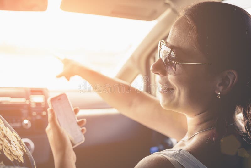 Fille de sourire employant l'application de navigateur de généralistes sur le smartphone pour diriger dans la voiture en vacances photos libres de droits Fille de sourire employant l'application de navigateur de généralistes sur le smartphone pour diriger dans la voiture en vacances photos libres de droits