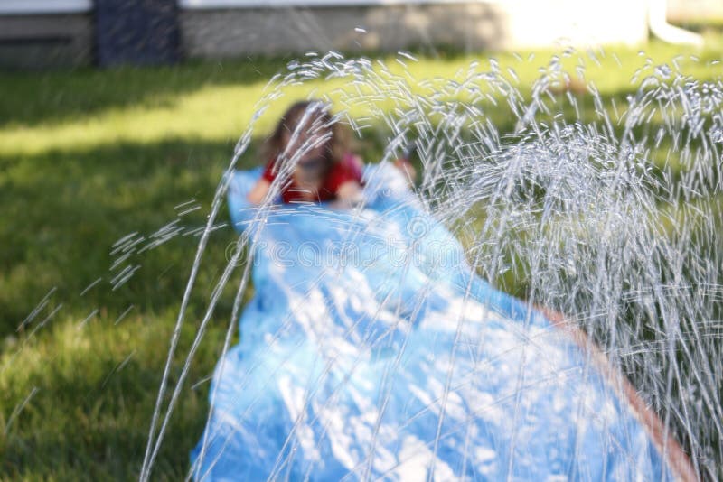 Fille de sourire glissant vers le bas un glissement et une glissière extérieurs foyer sélectif sur l'eau devant l'enfant image stock Fille de sourire glissant vers le bas un glissement et une glissière extérieurs foyer sélectif sur l'eau devant l'enfant image stock
