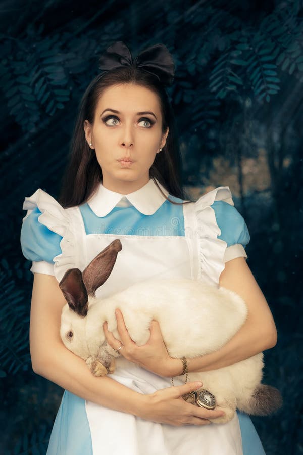 Fille drôle costumée comme Alice au pays des merveilles avec le lapin blanc photographie stock libre de droits Fille drôle costumée comme Alice au pays des merveilles avec le lapin blanc photographie stock libre de droits