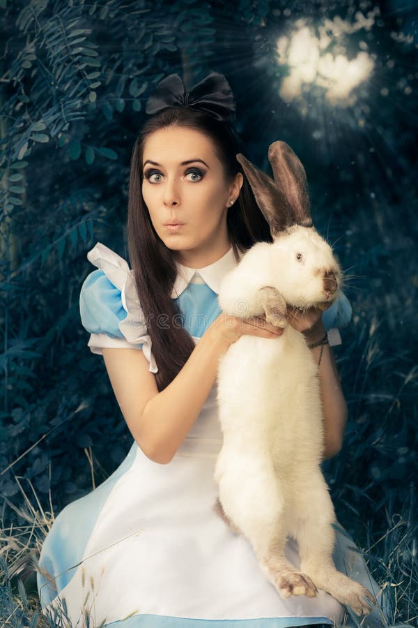 Fille drôle costumée comme Alice au pays des merveilles avec le lapin blanc images stock Fille drôle costumée comme Alice au pays des merveilles avec le lapin blanc images stock